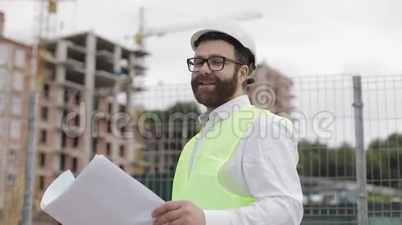 一位成功的年轻工程师或建筑师戴着白色头盔手里拿着施工图的肖像视频的预览图