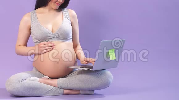 孕妇用瑜伽姿势在室内笔记本电脑上浏览互联网视频的预览图