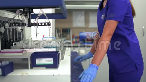 描绘了实验室年轻助理女士穿着蓝色制服戴着橡胶手套控制实验室药品生产视频的预览图
