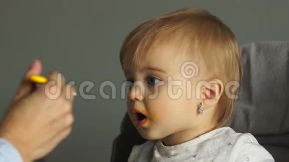 漂亮的蓝眼睛宝宝坐在高椅上尽职地吃着捣碎的蔬菜张开嘴妈妈给孩子喂奶视频的预览图