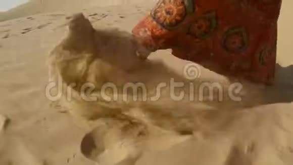 女孩赤着脚穿着五颜六色的裙子走在沙滩上把它扔到沙漠里视频的预览图