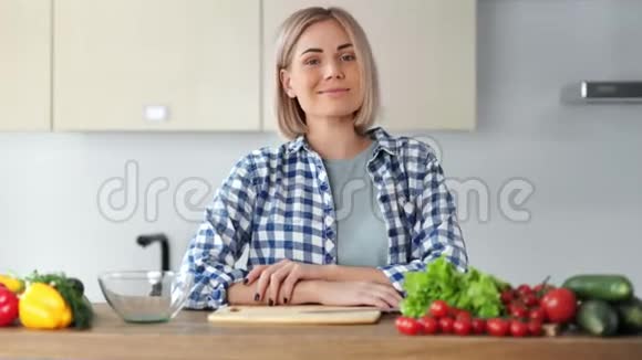 微笑休闲的年轻女子在厨房摆姿势周围是新鲜蔬菜中等特写视频的预览图