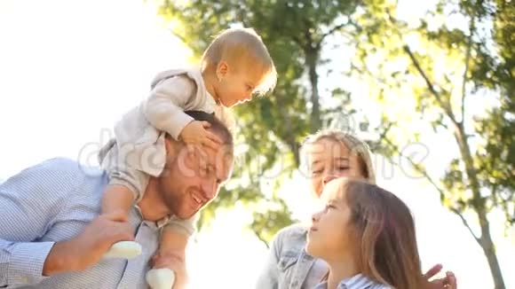 一对夫妇给两个年幼的孩子骑车微笑快乐的家庭在户外玩耍家庭一起享受视频的预览图