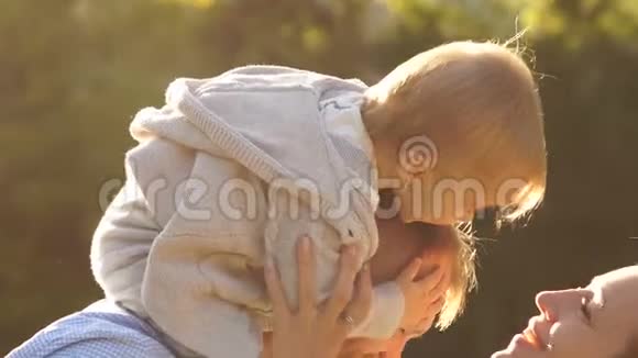 一岁的婴儿坐在父亲的肩膀上母亲伸出手来亲吻婴儿公园里的幸福家庭视频的预览图