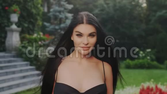 一位迷人的性感豪华的黑发女郎站在花园里穿着一件漂亮的黑色晚礼服领口敞开着视频的预览图