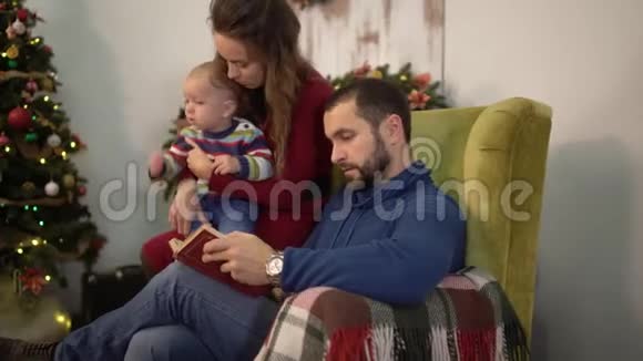 快乐可爱的一家人一起读书父亲坐在扶手椅上把小儿子抱在膝上视频的预览图