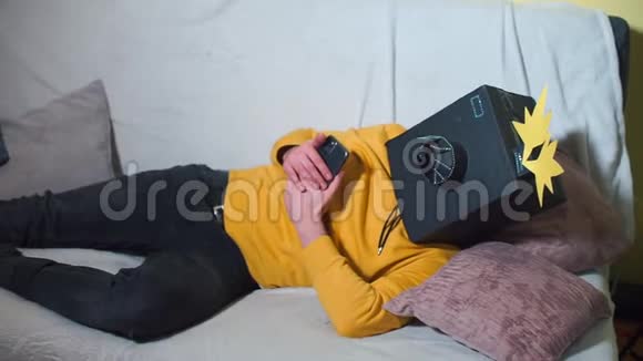 一个戴着相机面具的人躺在沙发上用智能手机视频的预览图
