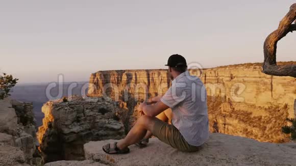 快乐兴奋的年轻成年游客坐在大岩石上观看大峡谷山脉上令人难以置信的日落景色视频的预览图