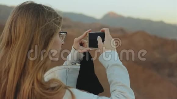 金发女人用智能手机拍摄大海女人呆在山顶慢慢地向地平线望去视频的预览图