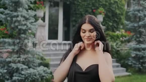 快关门漂亮害羞的黑发女孩站在花园里穿着一件漂亮的黑色晚礼服领口开着头发视频的预览图