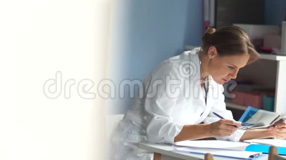医学和医疗保健概念一位可爱的成熟女医生坐在餐桌旁填写医疗文件视频的预览图