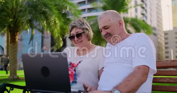 一对老夫妇在公园里坐在椅子上用笔记本电脑视频的预览图