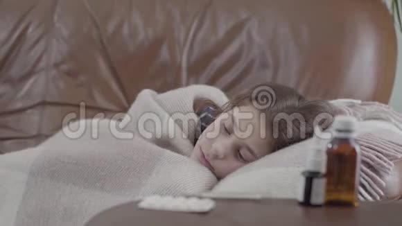 十几岁的生病女孩躺在沙发上盖着毯子在家里她很冷喷鼻剂药片和糖浆视频的预览图