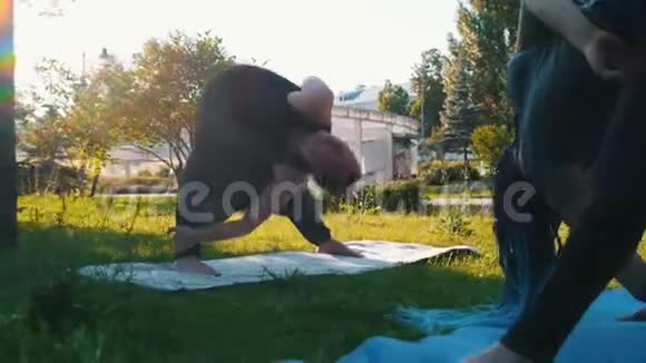 带着恐惧症的年轻女子在公园里和教练一起做瑜伽弯着腰摆姿势视频的预览图