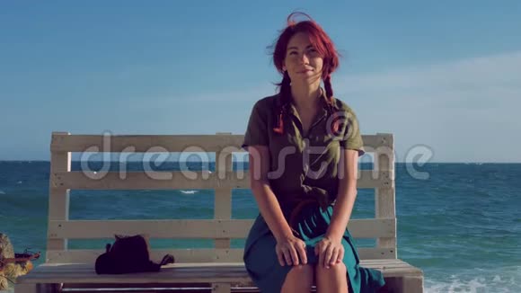 美丽的微笑红发旅行女孩坐在海边的长凳上梦想放松和享受生活视频的预览图