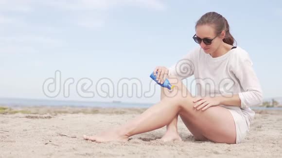 一个女人坐在海边她用晒伤膏擦她的腿视频的预览图