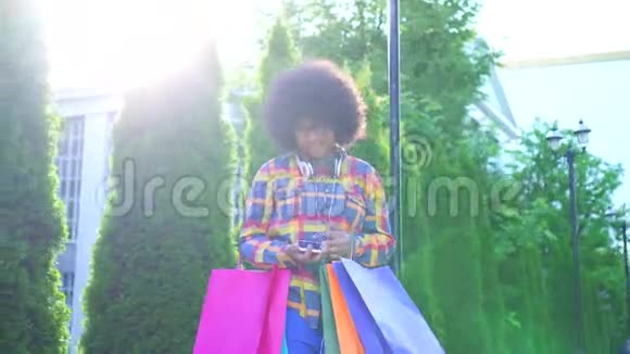 性格开朗的非洲裔美国妇女留着非洲发型购物后带着包裹使用智能手机视频的预览图