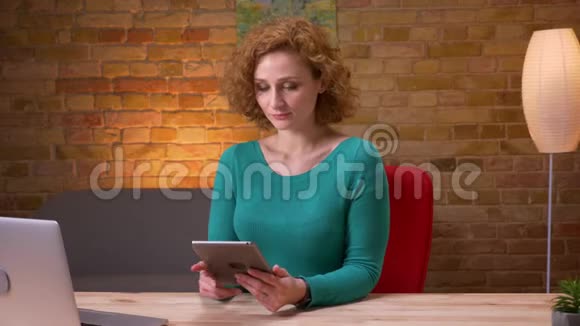 成年女商人在笔记本电脑前使用平板电脑并在室内拍摄蓝色屏幕的特写镜头视频的预览图