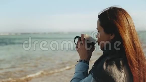 女人正在海滩上喝咖啡或茶海景蓝色女人看地平线快速视频慢动作4K视频的预览图
