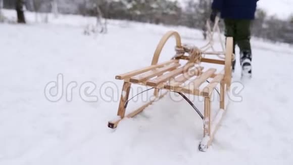 穿暖和衣服的可爱男孩在下雪的冬天拉木雪橇小男孩在公园里下雪跟踪视频的预览图