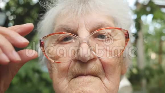 老妇人伸直眼镜看着照相机户外祖母的肖像关闭慢动作视频的预览图