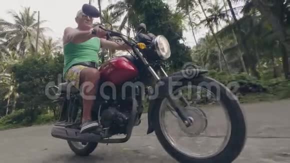 在阳光明媚的日子里养老金领取者骑摩托车在热带村庄骑摩托车在热带行驶的老人摩托车视频的预览图