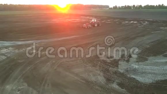 红拖拉机在夕阳下的上景下耕种大片农田土壤视频的预览图