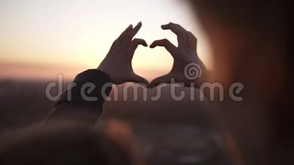 浪漫的年轻夫妇携手在屋顶上的太阳下形成了一种心形爱情和感情约会视频的预览图