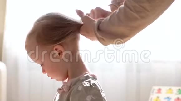 母亲给女儿梳头一个女人早上正在给她可爱的女儿梳头妈妈做她的小发型视频的预览图