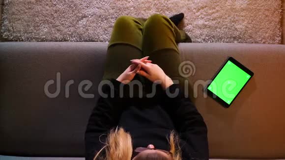 在平板电脑上发布漂亮女孩信息的特写镜头绿色屏幕在坐在沙发上时变得兴奋起来视频的预览图