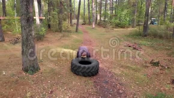 在秋天的森林里一个强壮的人在地上推着轮胎视频的预览图