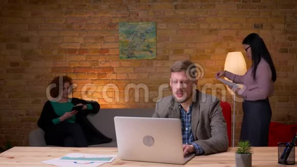 成人商人在笔记本电脑上打字的特写镜头兴奋不已与两位女同事在室内庆祝视频的预览图