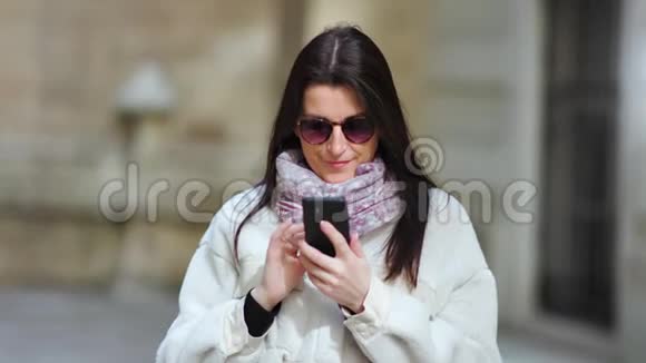 带围巾和保暖外套的中等身材时尚的微笑女性使用智能手机输入信息视频的预览图