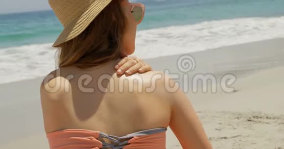 白种人女性在海滩4k时在身体上涂抹乳液的后视图视频的预览图