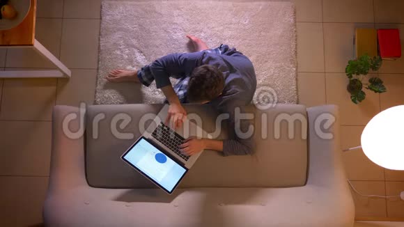 一位年轻商人的特写镜头他在室内坐在地板上在笔记本电脑上制作一张图表视频的预览图