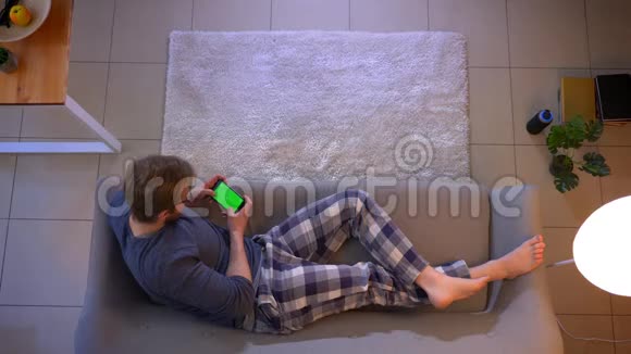 一位身着休闲服的年轻男性在手机上观看一则广告的特写镜头绿色屏幕躺在手机上视频的预览图