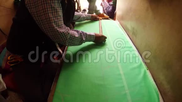 裁缝的双手在绿色布脚上画图案在背景印度缝纫车间拉贾斯坦邦比坎纳拥挤的街道上画图案视频的预览图