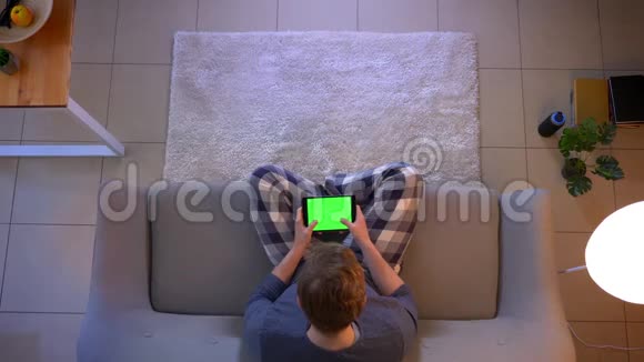 在平板电脑上年轻时穿着随意的男性短信坐在平板电脑上屏幕上显示着绿色的色度视频的预览图