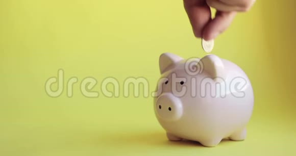 男人把硬币放在黄色背景上猪形的储蓄罐里视频的预览图