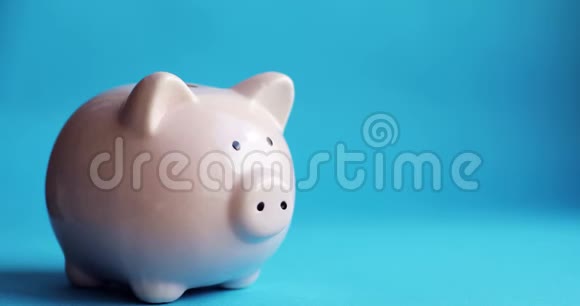 男人把硬币放在蓝色背景上猪形的储蓄罐里视频的预览图