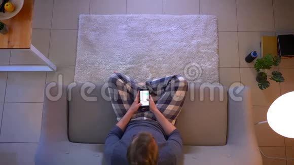 在舒适的室内沙发上坐着时一位穿着随意的年轻男性在网上发短信视频的预览图