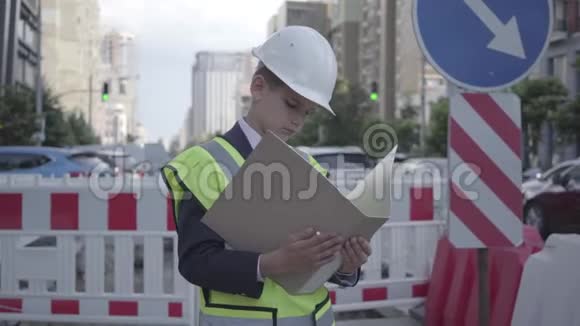 肖像小男孩戴着安全设备和建筑工人头盔阅读建筑计划控制工作繁忙视频的预览图