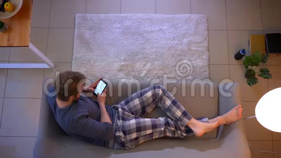 在舒适的家中躺在沙发上的年轻人穿着随意的男性短信特写镜头视频的预览图