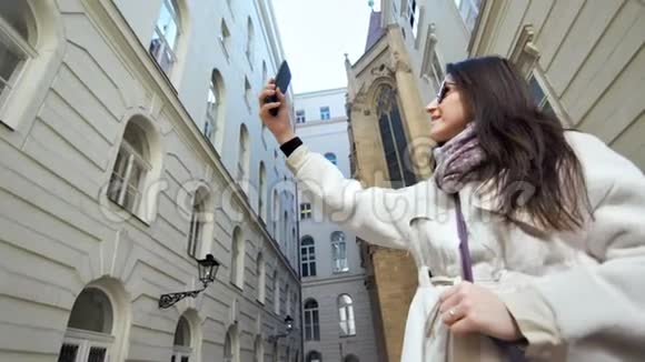 使用智能手机在欧洲历史建筑附近自拍的快乐时尚女游客视频的预览图