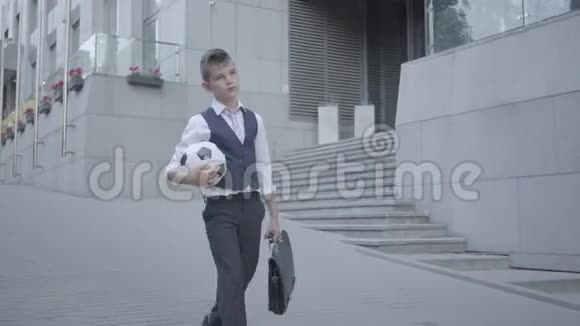 严肃的穿着得体的男孩走在街上手里拿着足球和钱包严肃的孩子视频的预览图