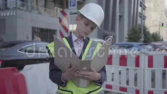 肖像小男孩戴着安全设备和建筑工人头盔阅读建筑计划控制工作繁忙视频的预览图