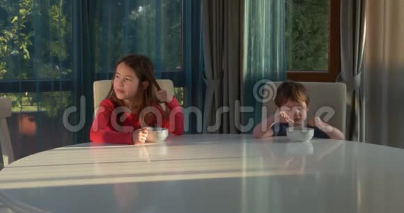 快乐的孩子们早餐吃玉米片兄妹俩早餐吃玉米片坐在餐桌旁视频的预览图