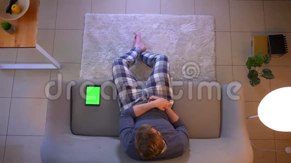 年轻的穿着随意的男性看电视使用平板电脑和绿色屏幕坐在沙发上的特写镜头视频的预览图
