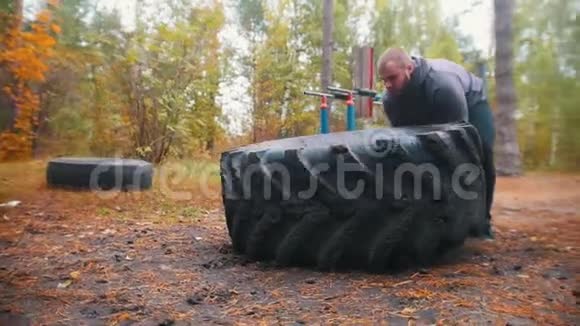 一个纹身的强壮的健美男子推着轮胎在地上训练在秋天的森林视频的预览图