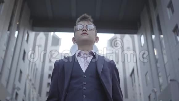 肖像可爱衣着考究的男孩戴着眼镜站在街上看着镜头严重的孩子面前视频的预览图